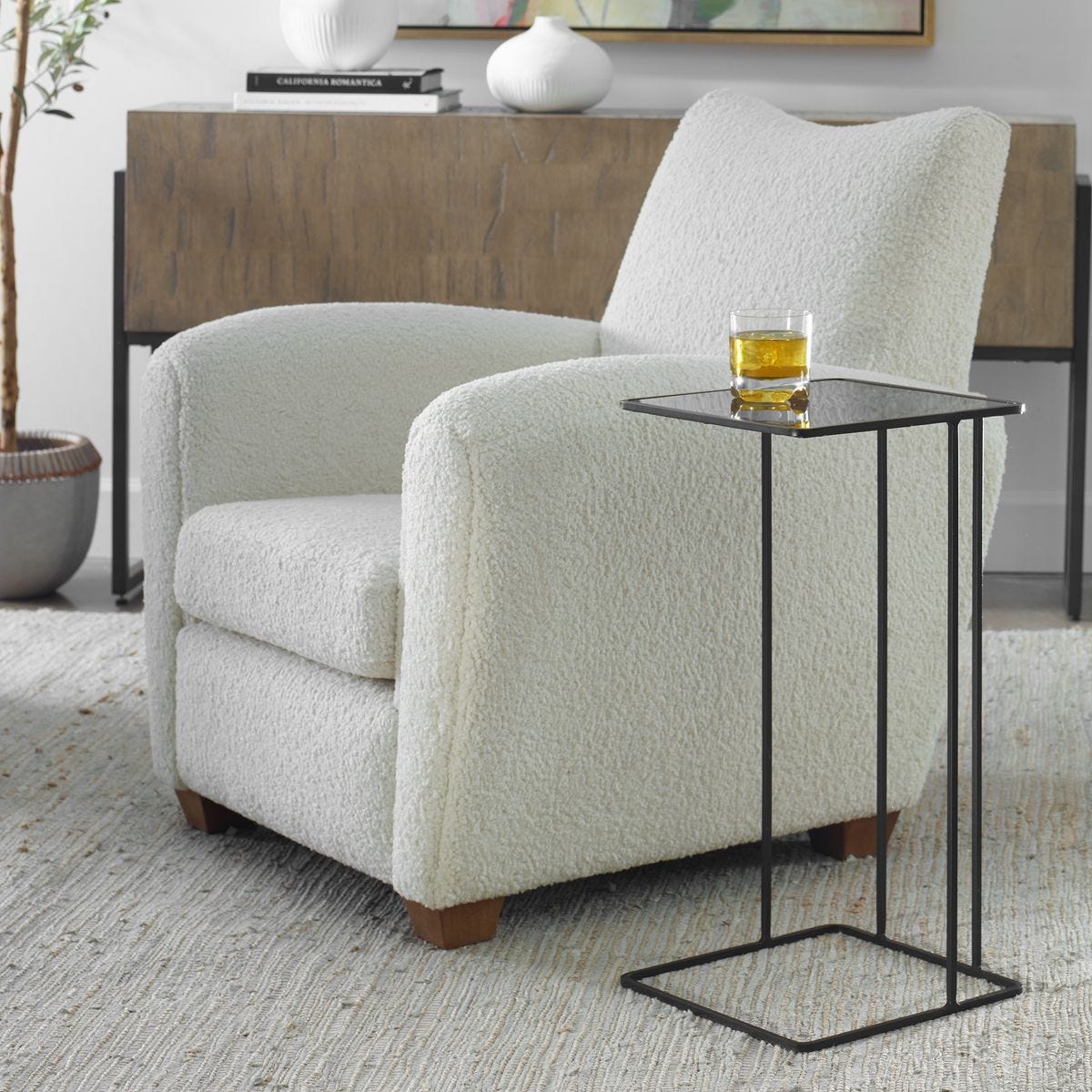 Light gray armchair with a small black side table holding a glass of amber liquid, in a room setting.