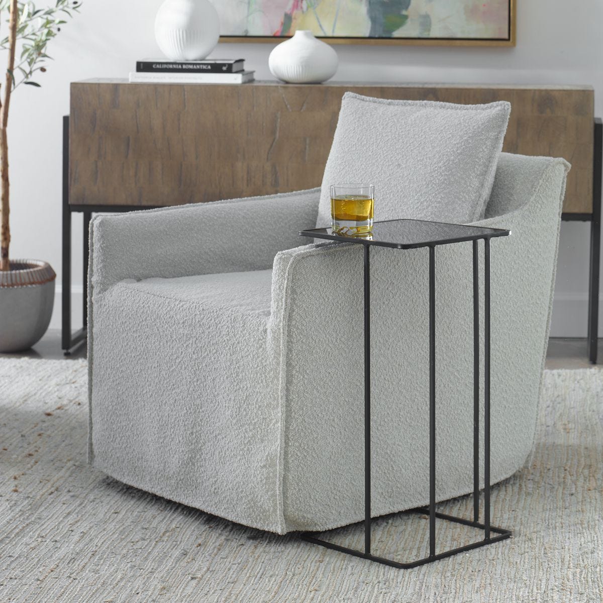 Gray armchair with a small black table holding a glass of yellow liquid, in a room setting.