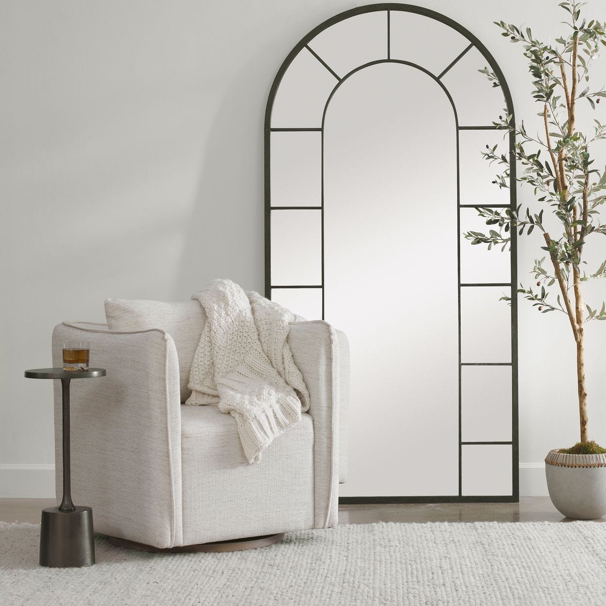 Decorative arch mirror in a room with a chair, side table, and plant.