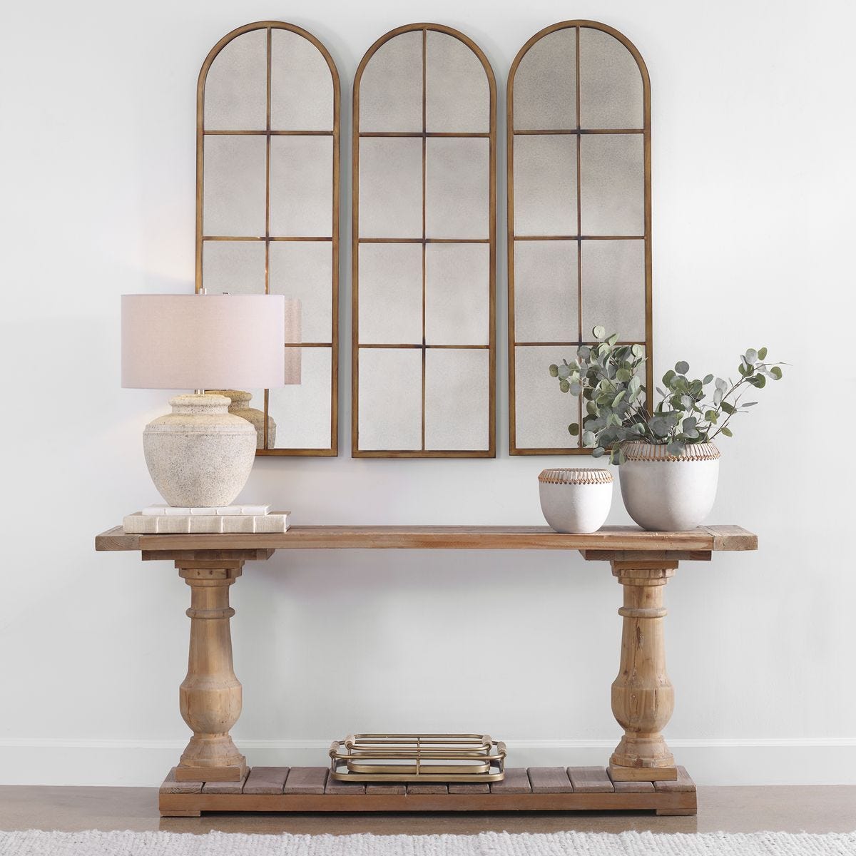 Wooden console table with decorative items against a wall with three arched mirrors.