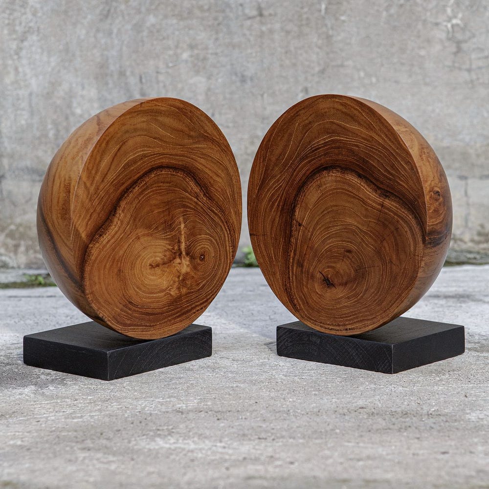 Two wooden sculptures on black stands against a concrete background.