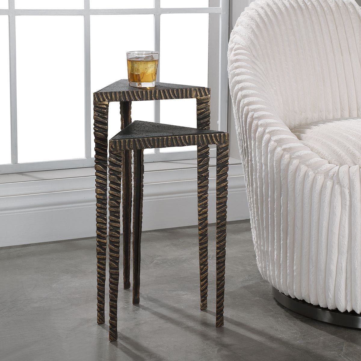 Set of two woven side tables with a glass of juice on top, next to a white upholstered chair.