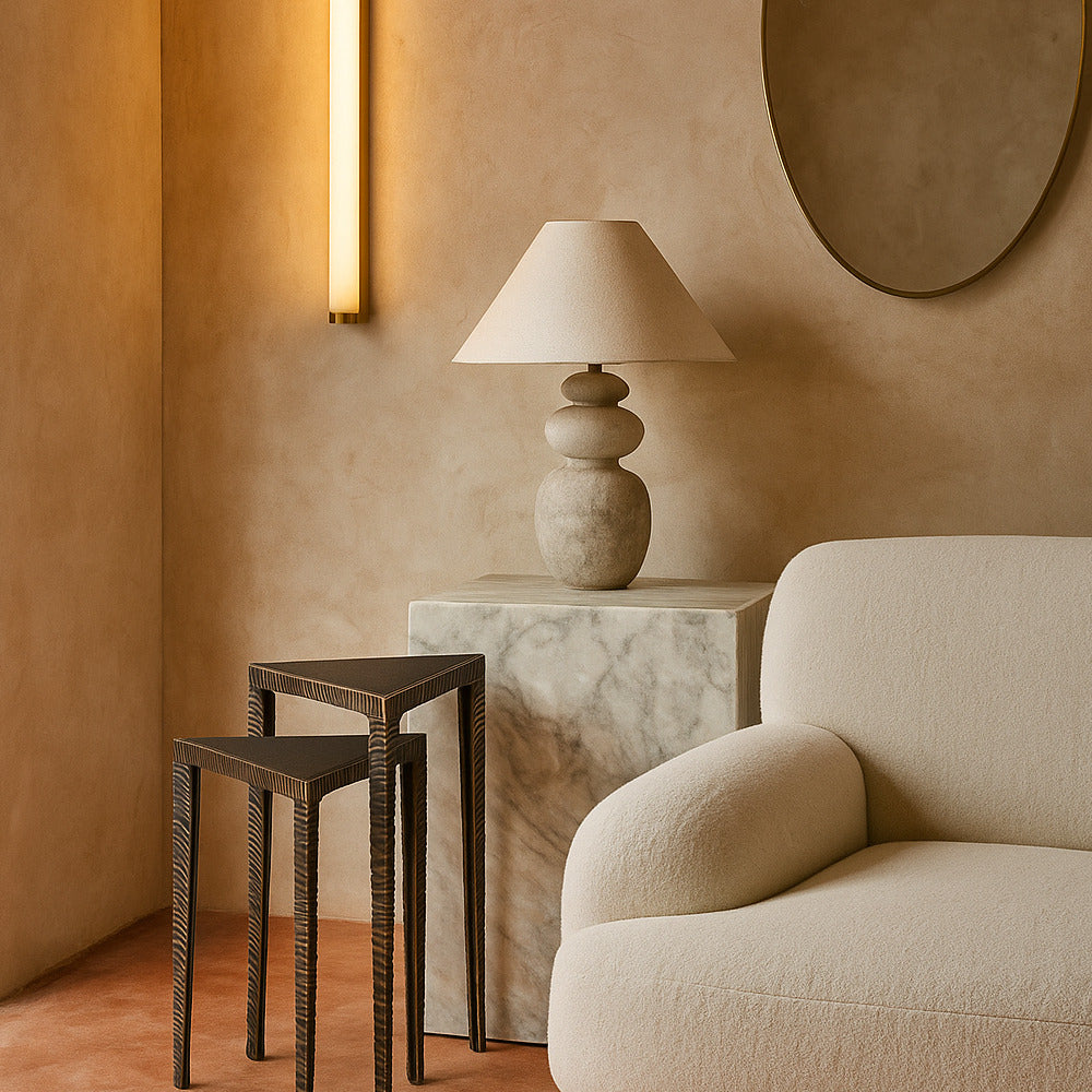 Beige armchair with a lamp and side tables against a beige wall.