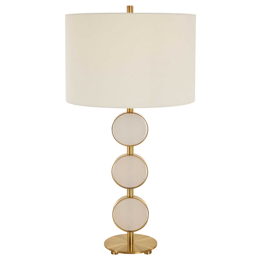 White and gold table lamp with round circle on a console with books and accessory.