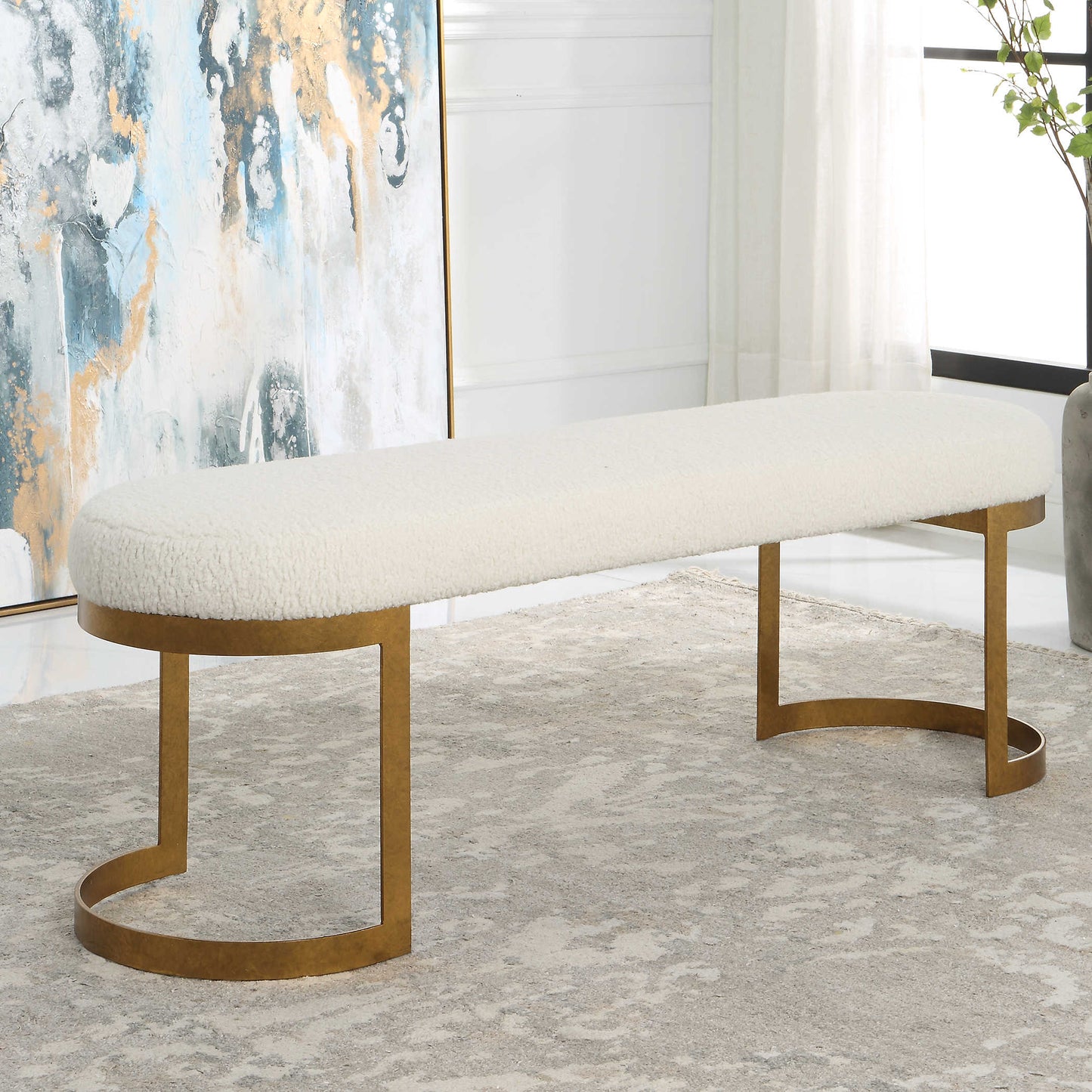 White and gold bench in living room with abstract painting in the background in blue and yellow.