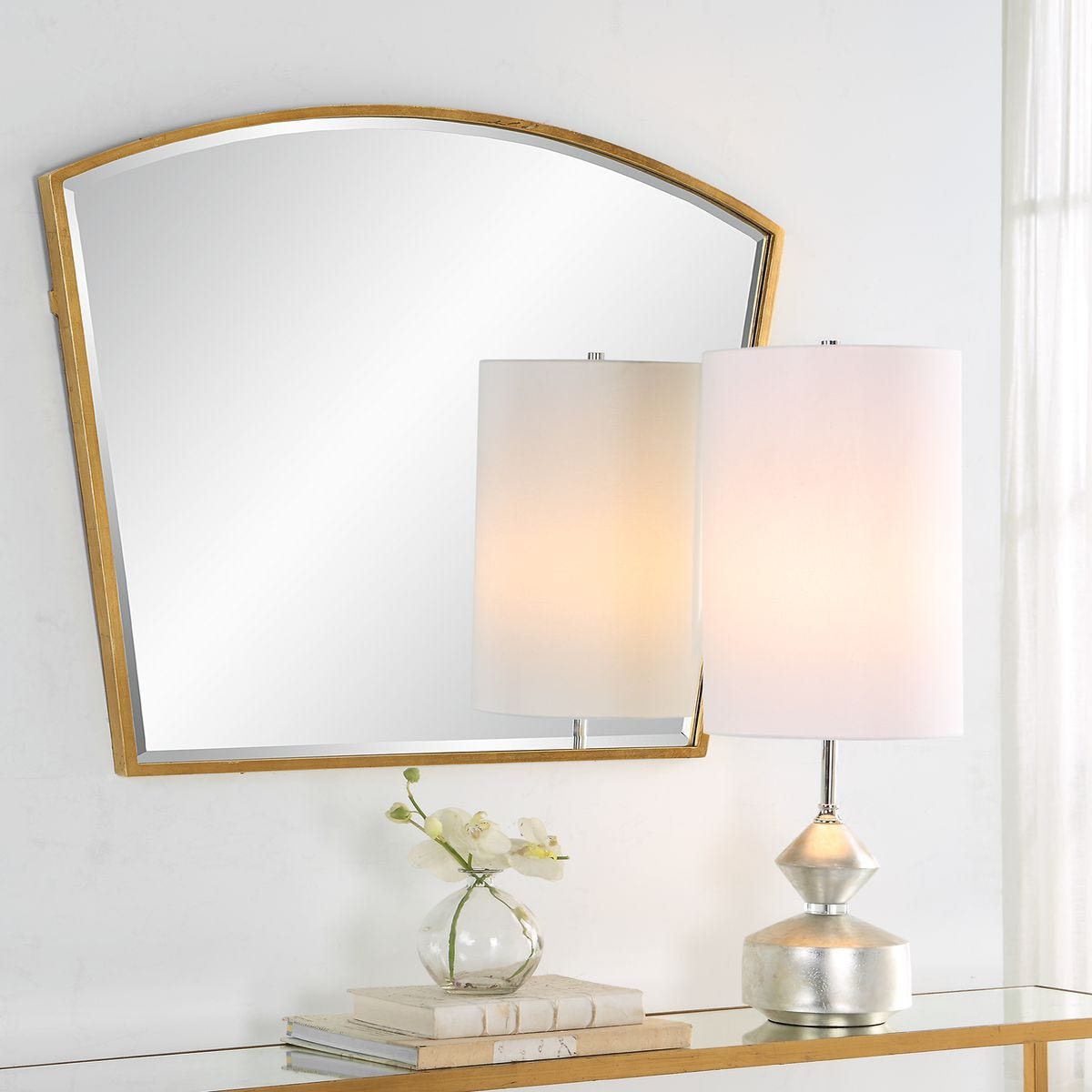 Decorative mirror with a lamp and small plant on a shelf against a white wall.