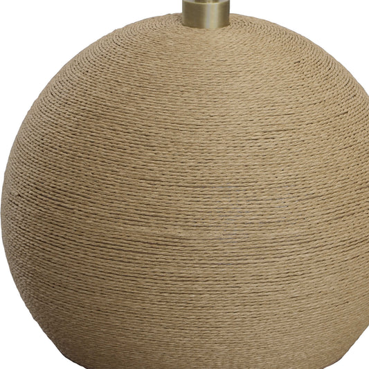 Satin brass stem with woven rattan base of a beach floor lamp beside white decorative chair.