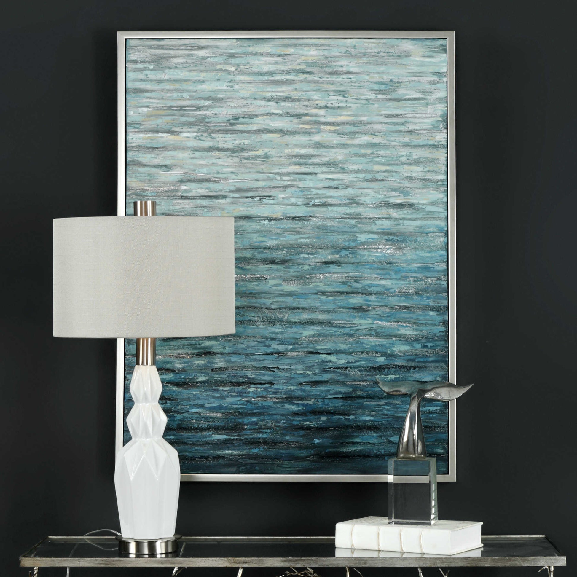 Blue textured print of waves on water that are abstract behind a white lamp and decorative sculpture on a gray background.