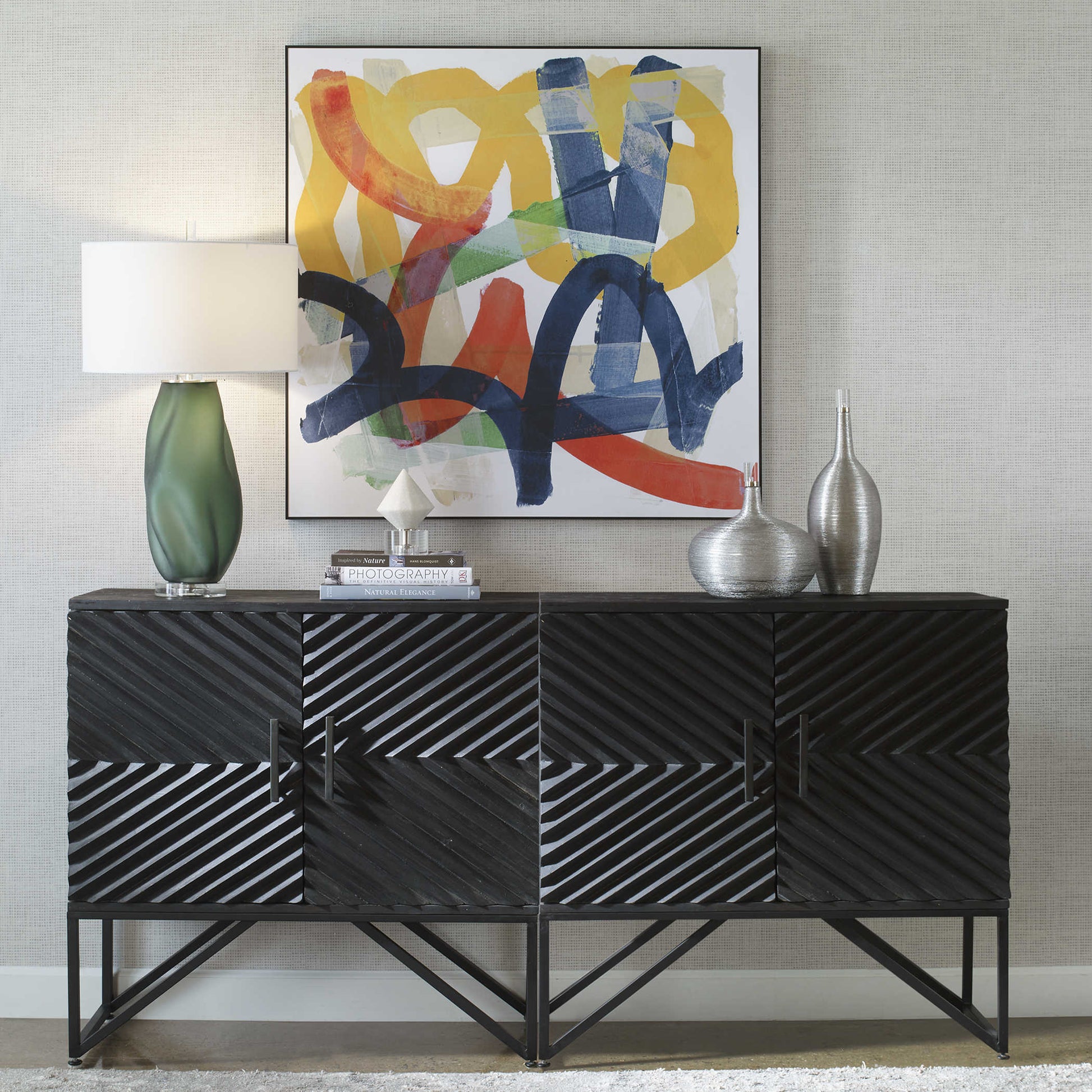 Straight up shot of a colorful and abstract piece of art behind a modern black console with an accent lamp and sculptures.