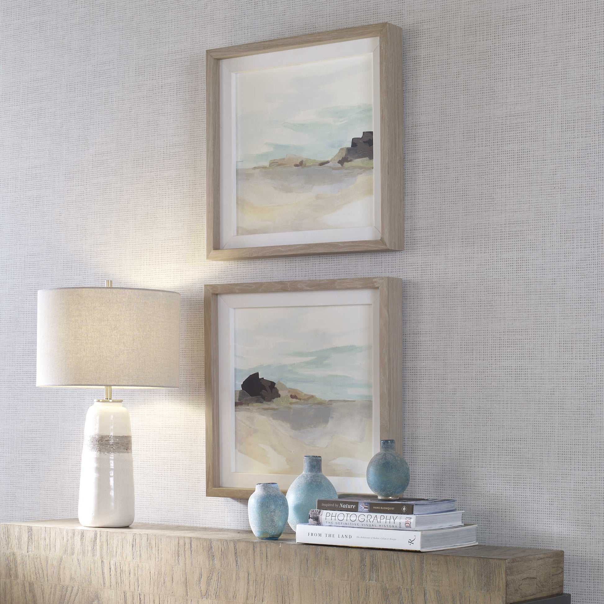 Vertically stacked prints above a console near a lamp.