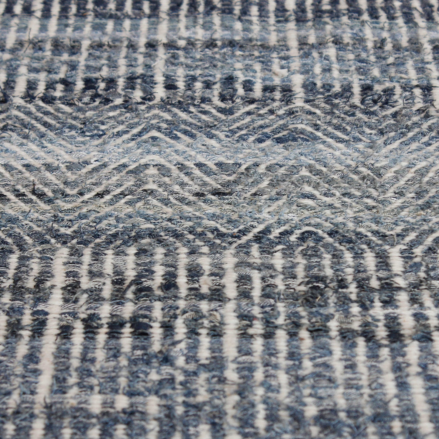 Macro shot of a geometric wool rug with denim fibers and light green and gray fibers.