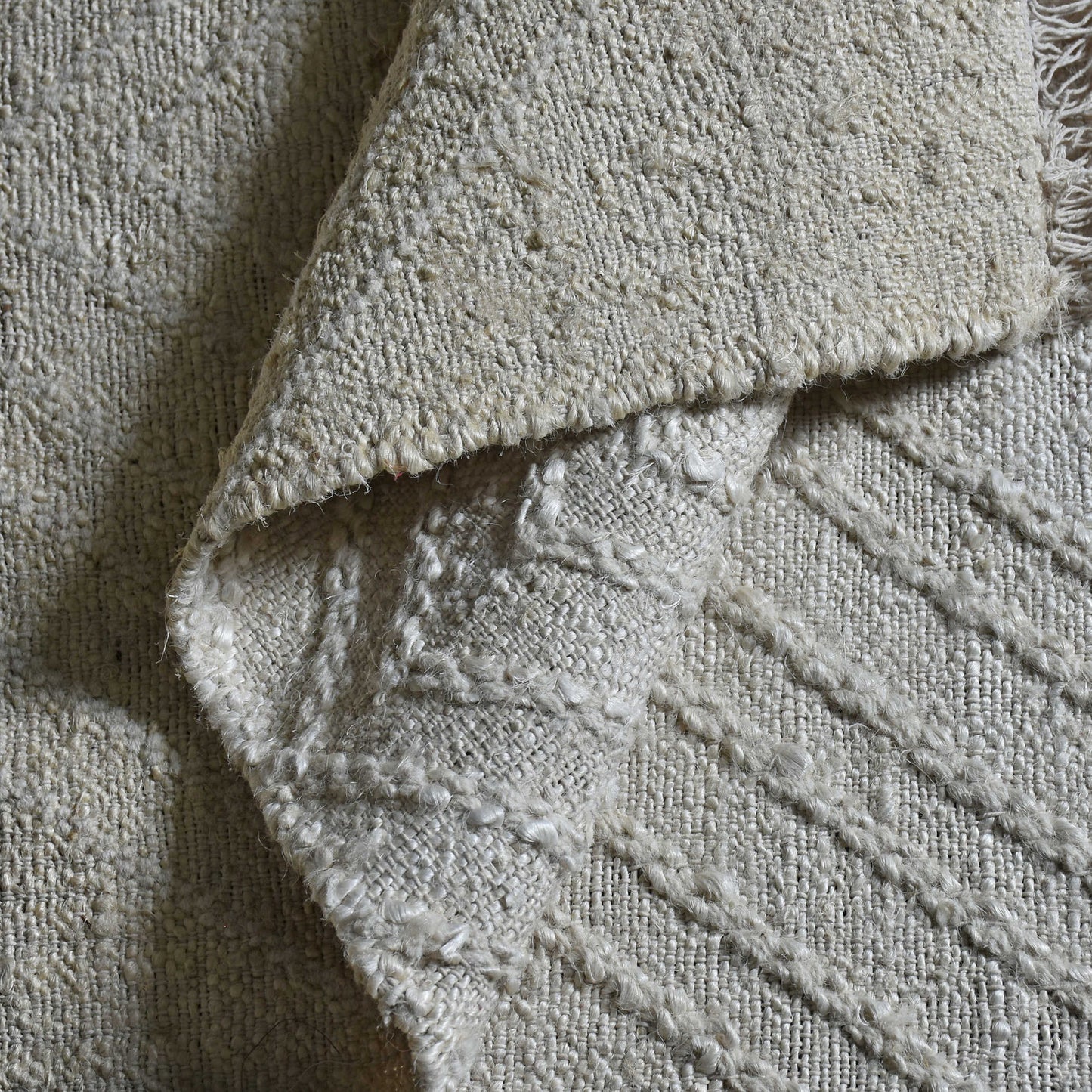 Close up shot of the rug folded up so you can see the woven texture of the off-white hemp.