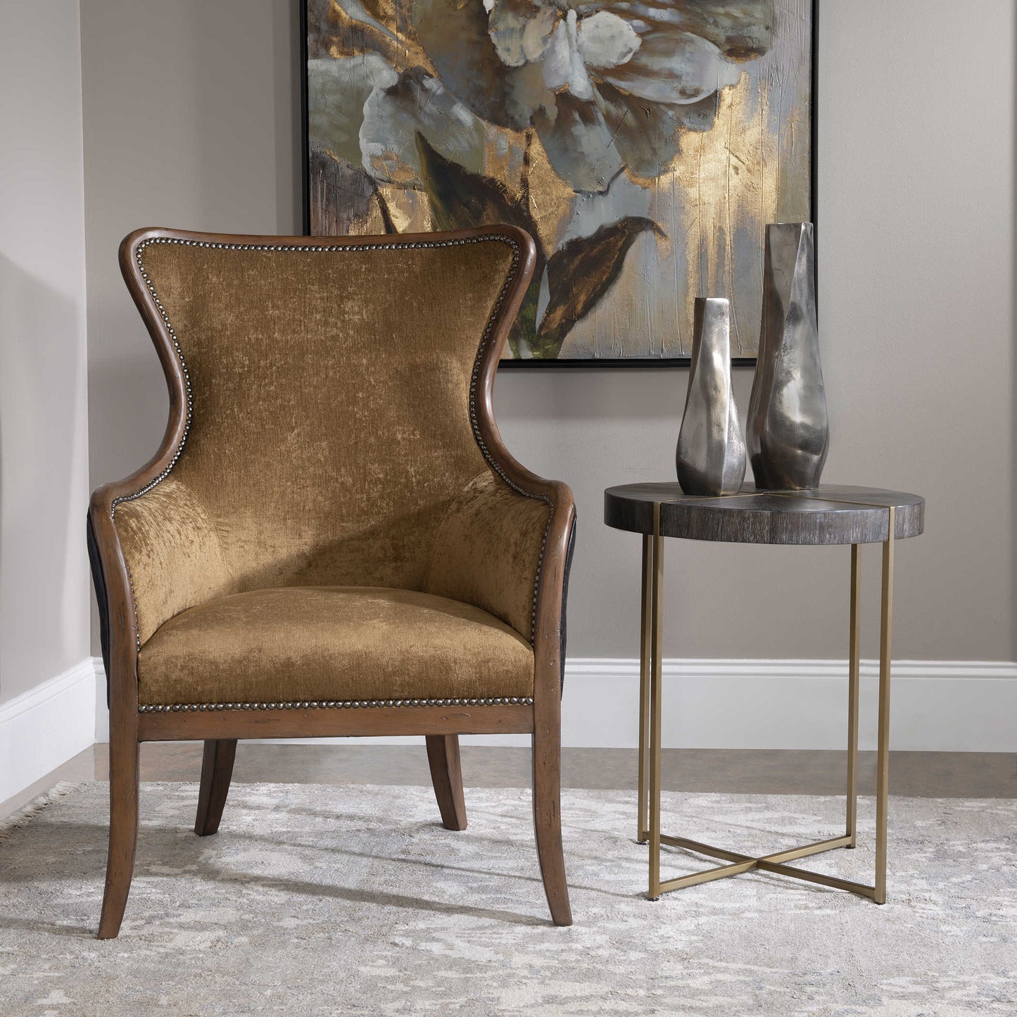 White rug, tan chair, a round dark wood side table with two silver distressed sculptures in a traditional living room.