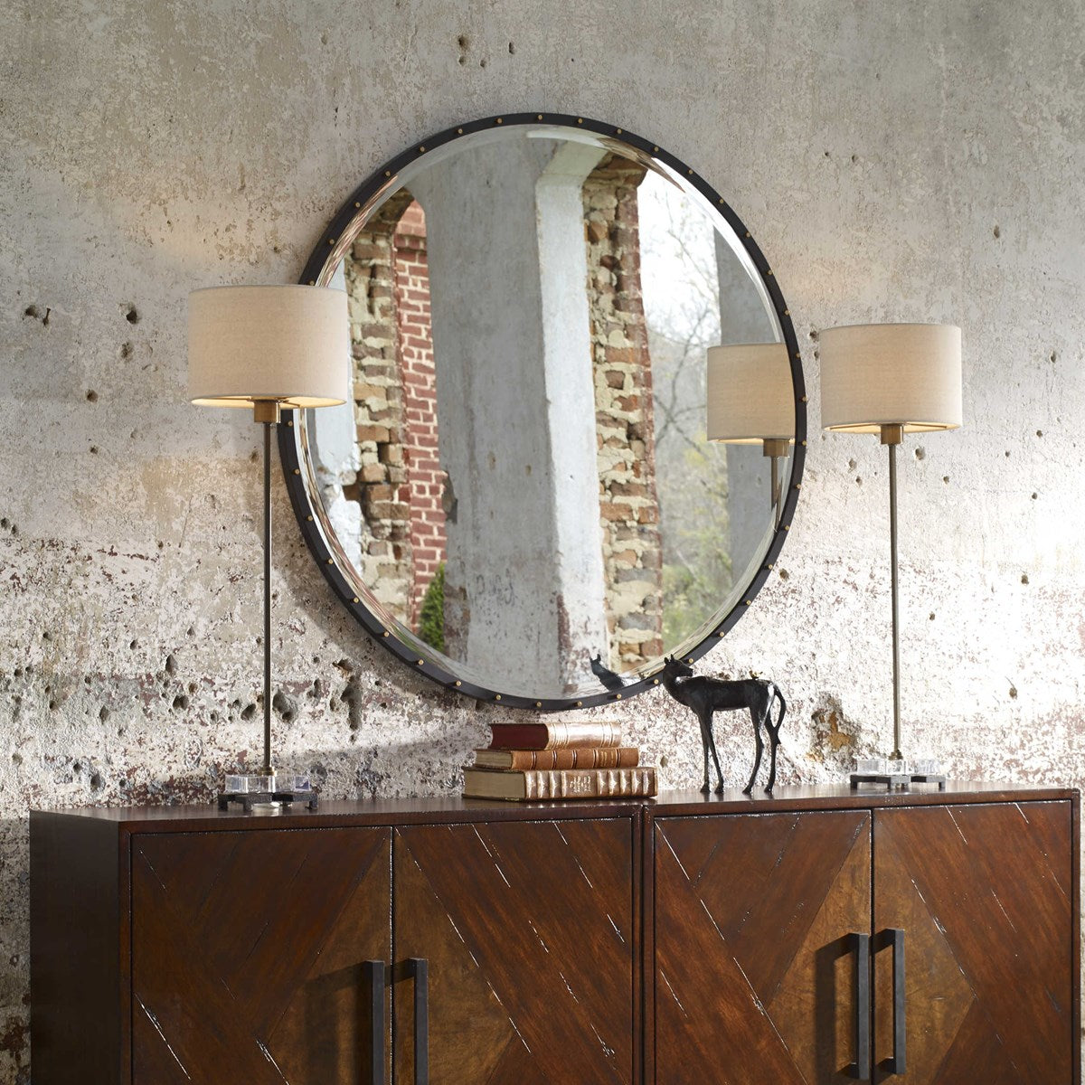 Rustic Antique Industrial round mirror with gold accent screw caps above a wood console table with decorative books and table lamps.