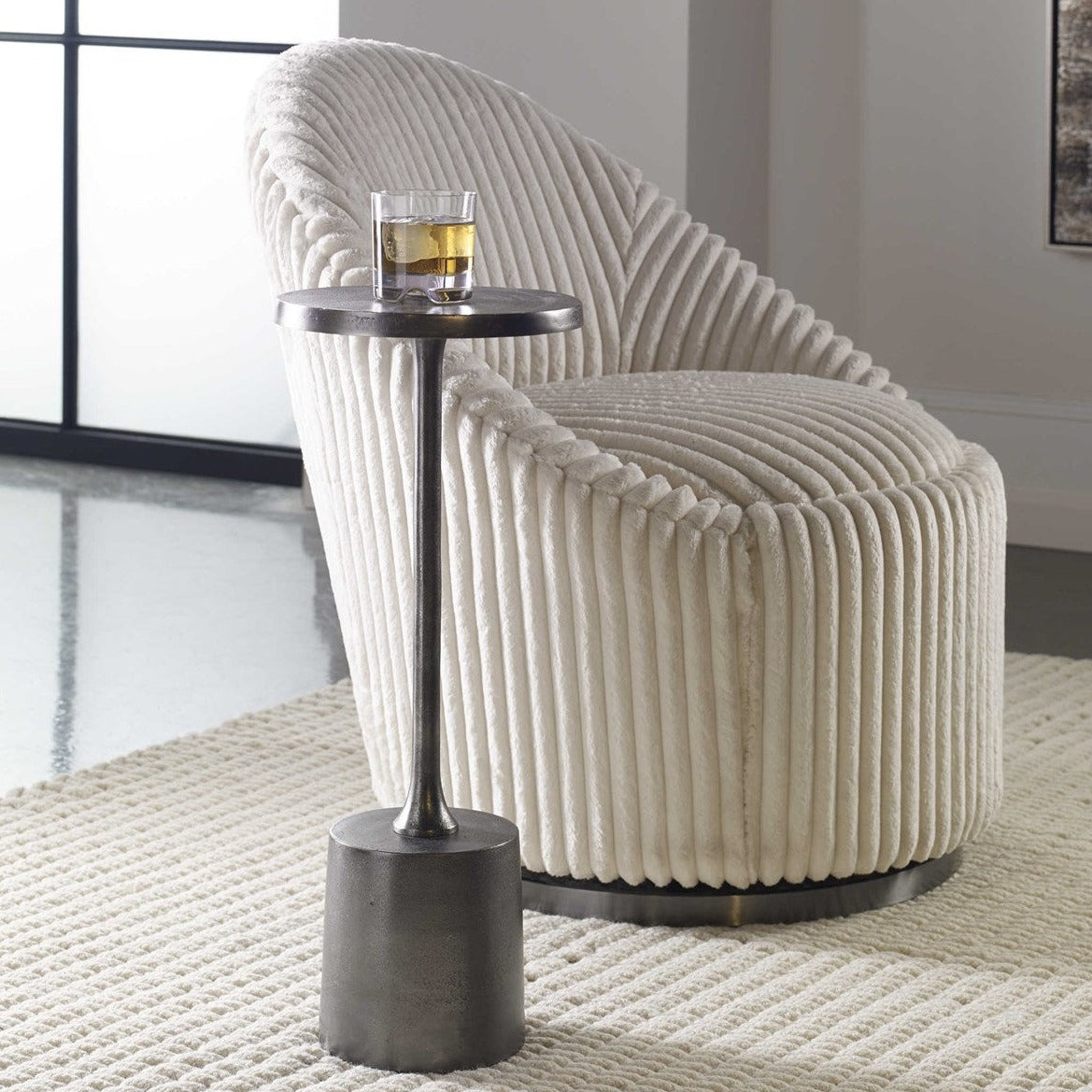 Small antique outdoor nickel drink table with a glass of scotch sitting on top in a trendy living room next to a chair.