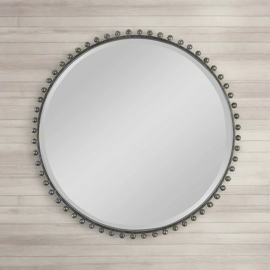 Black iron mirror that is round with decorative spheres / balls around the exterior in a living room above a black console.