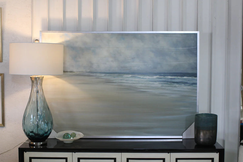 Coastal Home Artwork on top of a blue glass lamp and a console. 