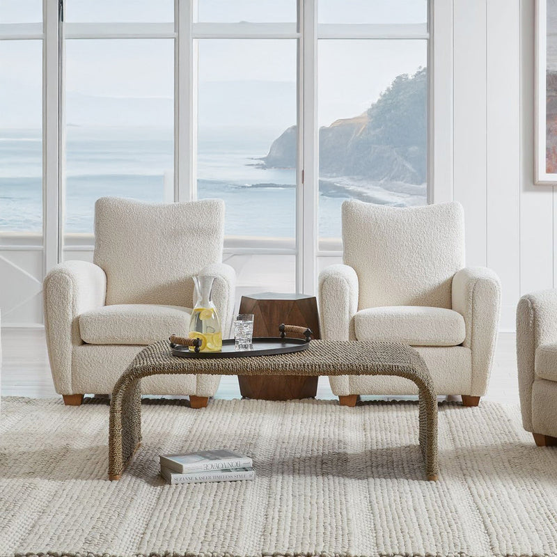 Coastal living room with rattan coffee table and white decorative chairs.