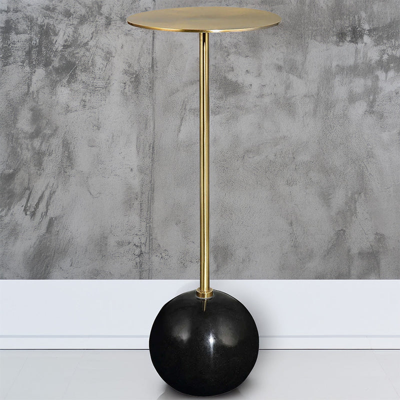 Drink table with black base and brass stem on a concrete wall. 