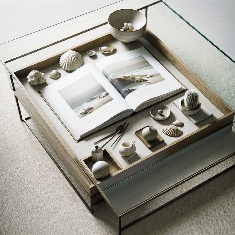 Glass coffee table that is styled with coastal book and bowl with shells.