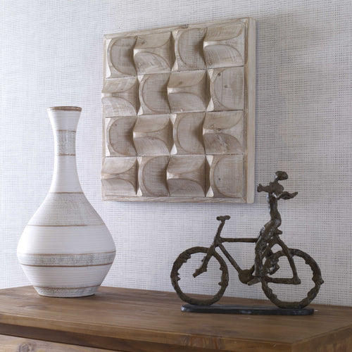 White wood carved wall art above wood console and white vase. 