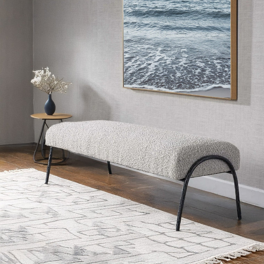 White coastal bench below ocean art and flower case in a living room.