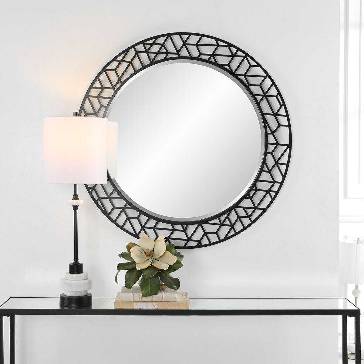 Decorative round mirror with geometric frame on a white wall above a console table.