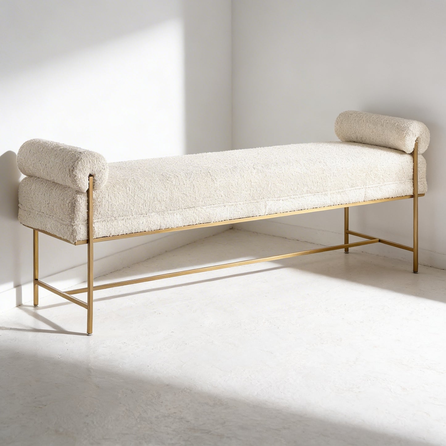 White boucle upholstered bench with gold frame on a white floor and wall