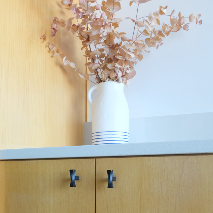White vase with dried flowers on a kitchen counter with black twisted cabinet knobs.
