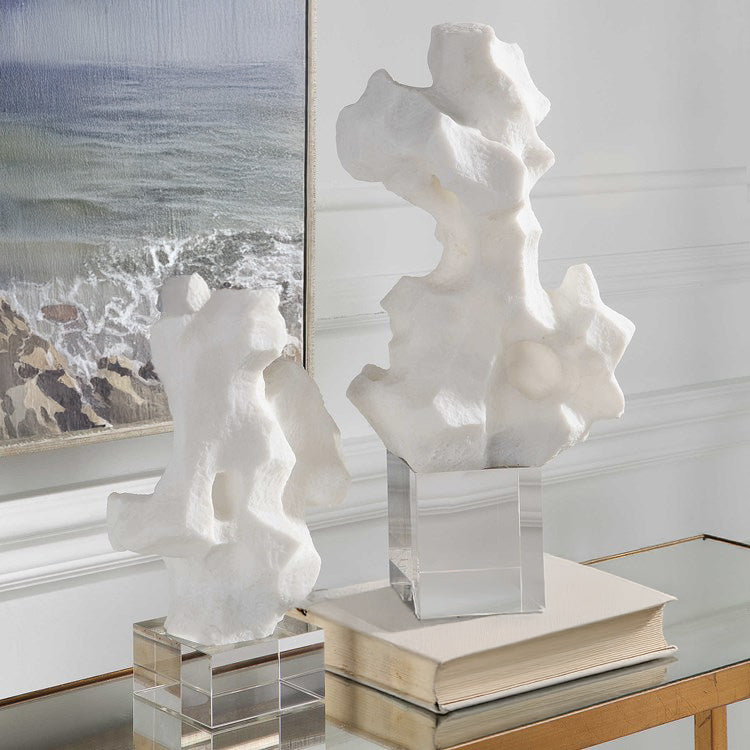 Two abstract white sculptures in front of coastal art on a brass console.