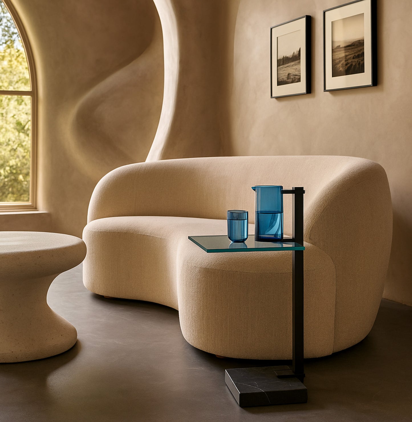 Beige sofa with a small table and blue glasses in a room with wavy beige walls and framed pictures.