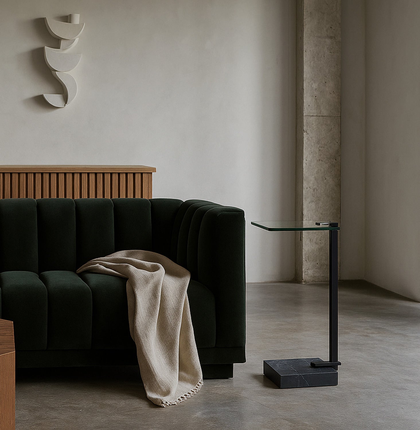 Modern living room with a dark green sofa, beige blanket, and a glass side table.