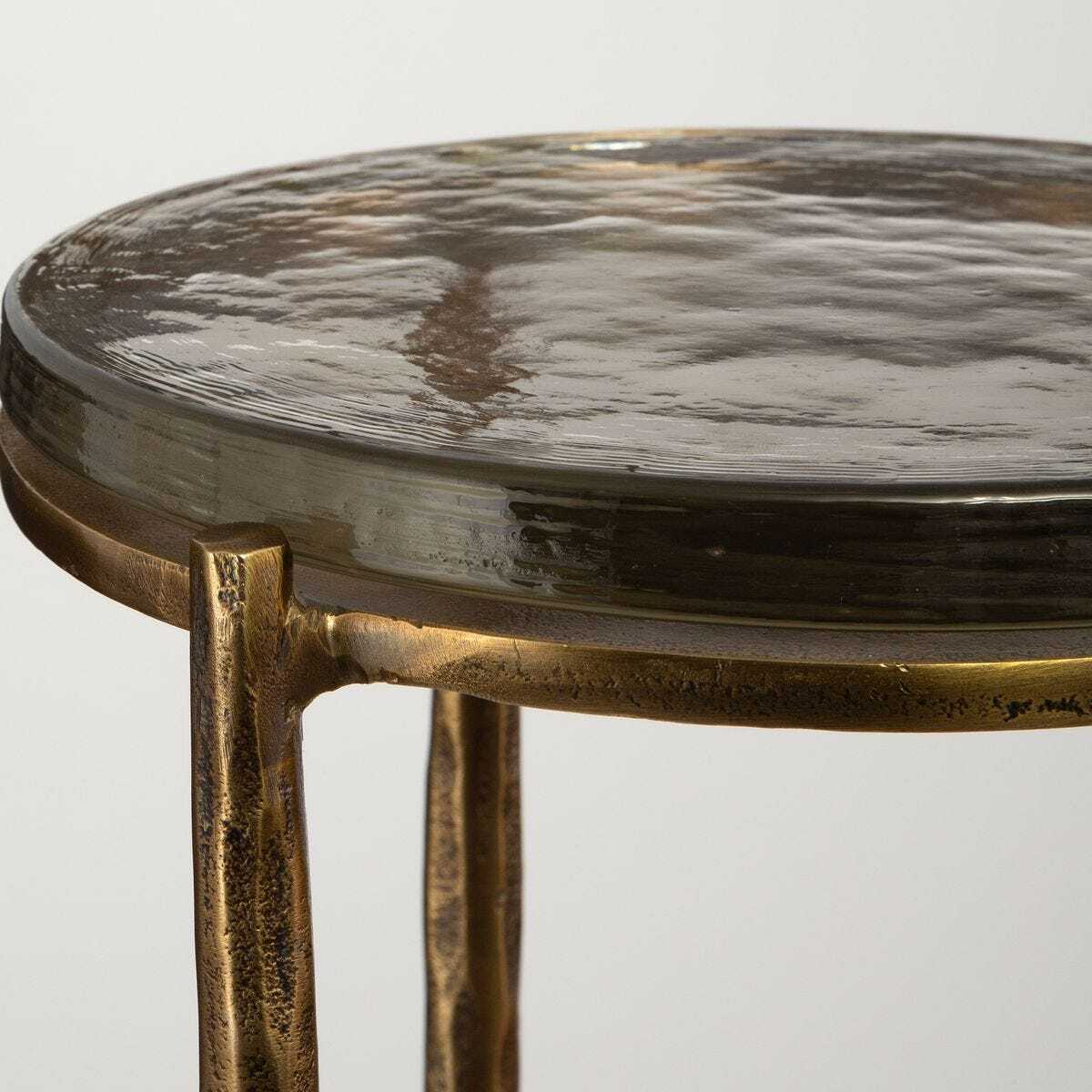 Round metal table with textured surface and bronze legs on a light gray background