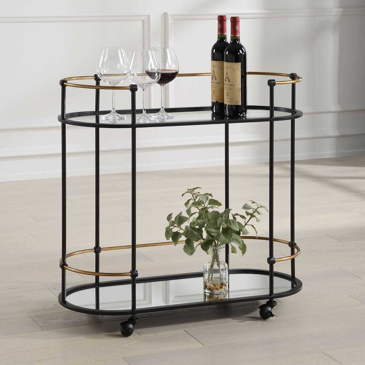 Bar cart with wine bottles, glasses, and a plant on a wooden floor.