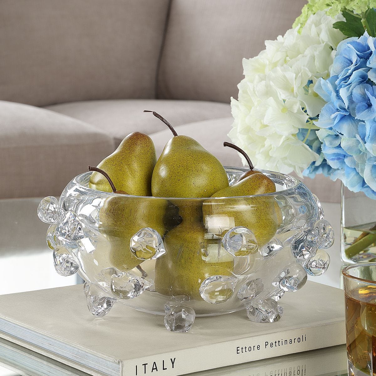 Clear glass bowl with pears on a table with flowers in the background