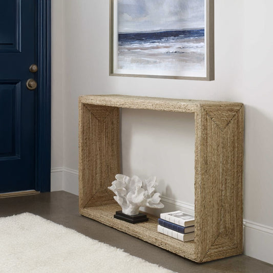 White coral statue in entryway on rattan coastal console table with ocean art hung above and a white rug.