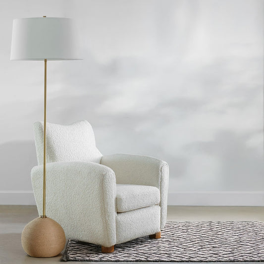 Satin brass stem with woven rattan base of a beach floor lamp beside white decorative chair.