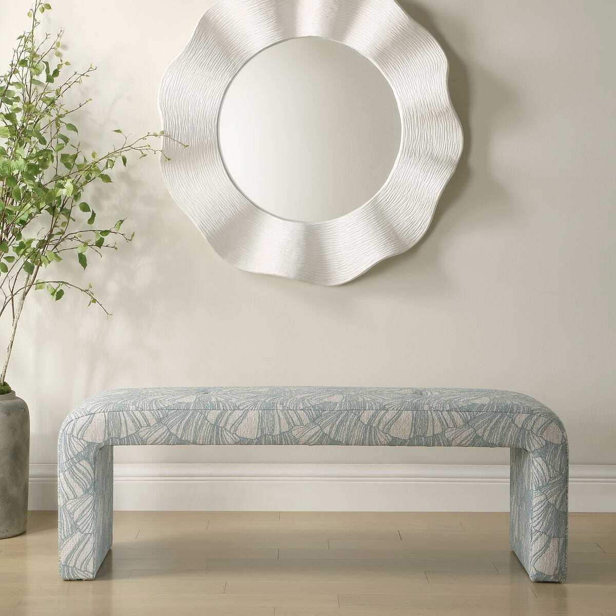 Decorative bench with leaf pattern in front of a textured wall mirror.