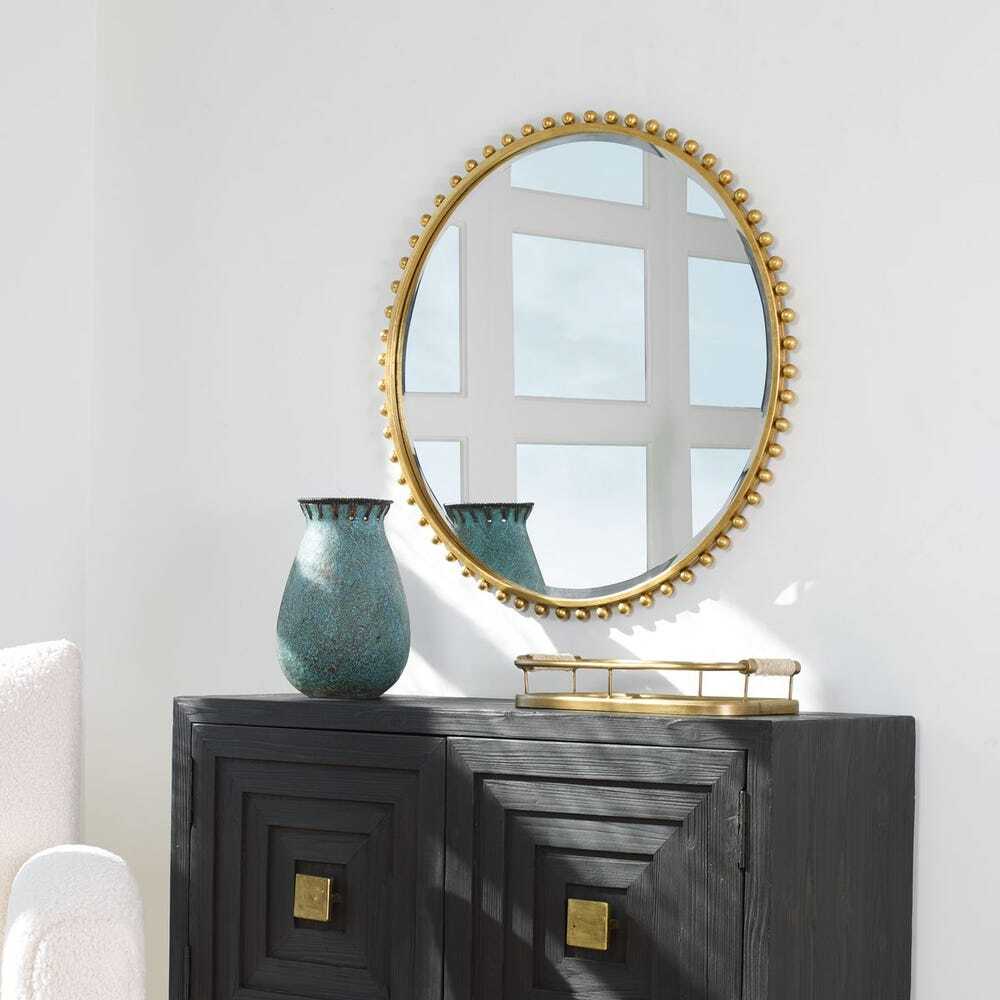 Round gold-framed mirror on a dark wooden console table with decorative items.