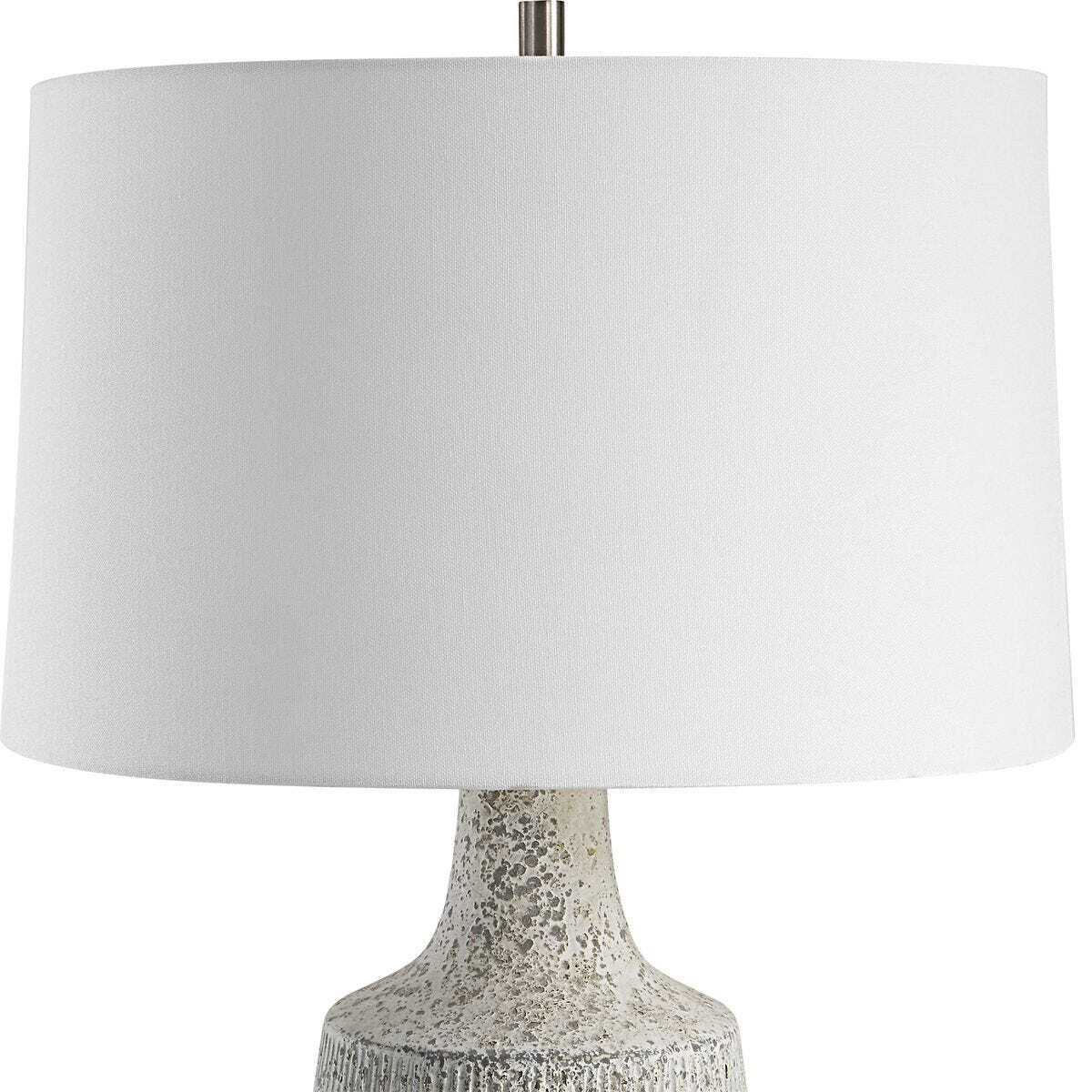 A table lamp with a large white fabric drum shade and a textured, metallic silver and white ceramic base, shown against a plain white background.