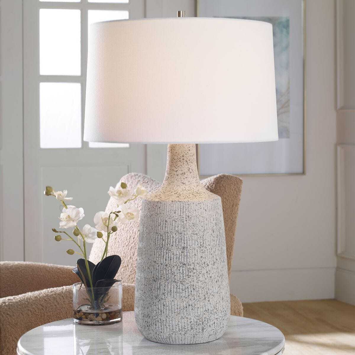 Table lamp with textured base and white shade on a table in a room setting.