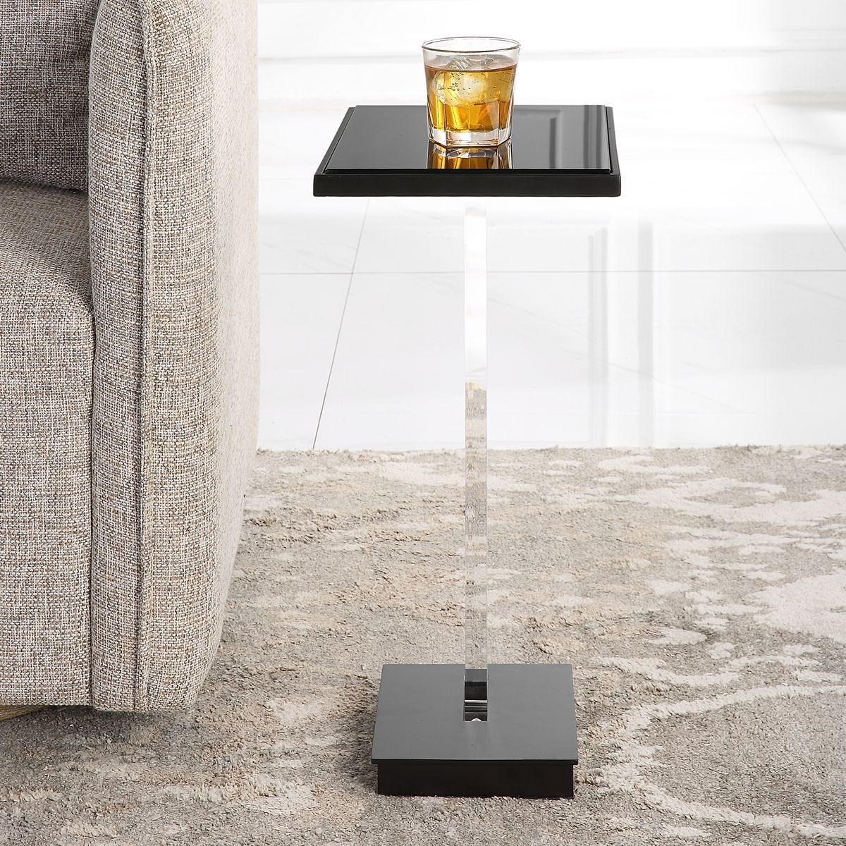 Modern black side table with a glass of whiskey next to a gray sofa.