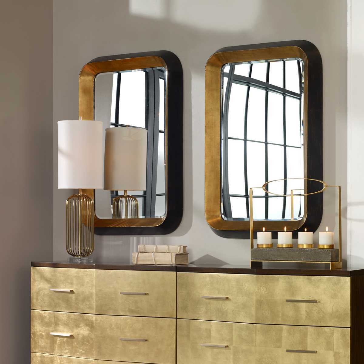 Gold and black mirrors on a dresser with decorative items.