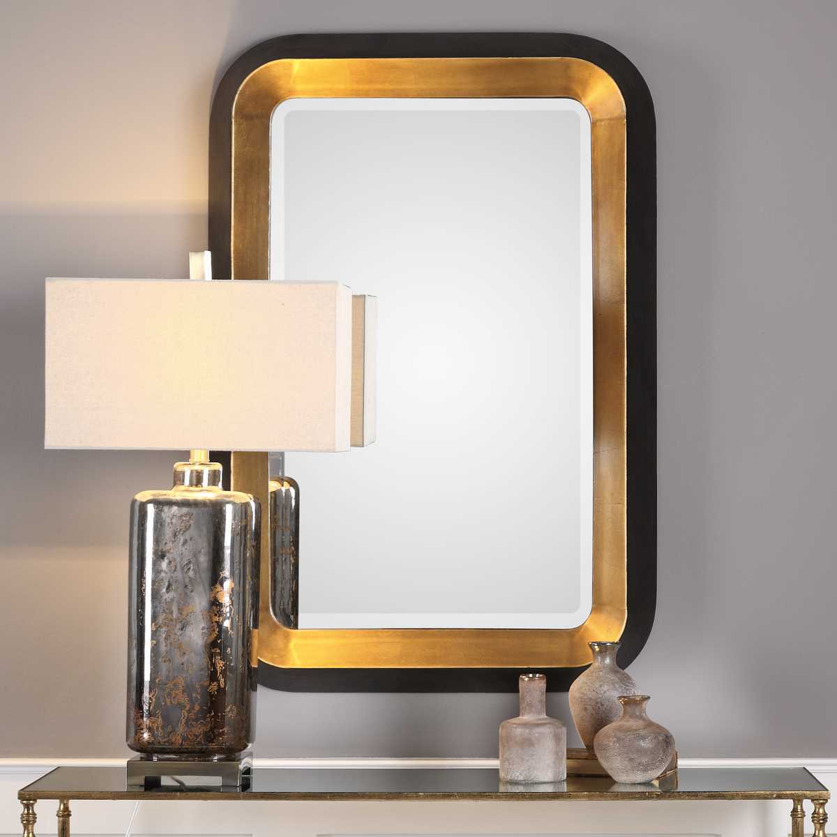 Decorative table with a lamp, mirror, and vases against a gray wall.