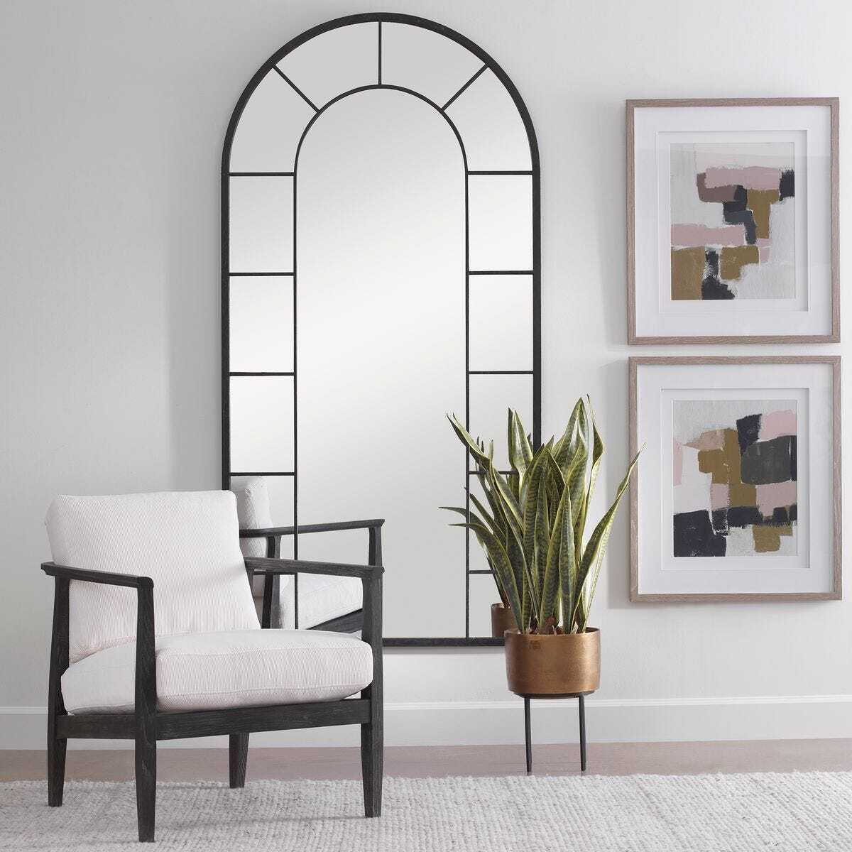 Modern interior with a white armchair, arch mirror, and abstract art on a light gray wall.
