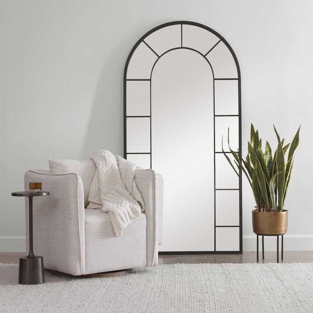 Arched mirror in a room with a chair, plant, and small table.
