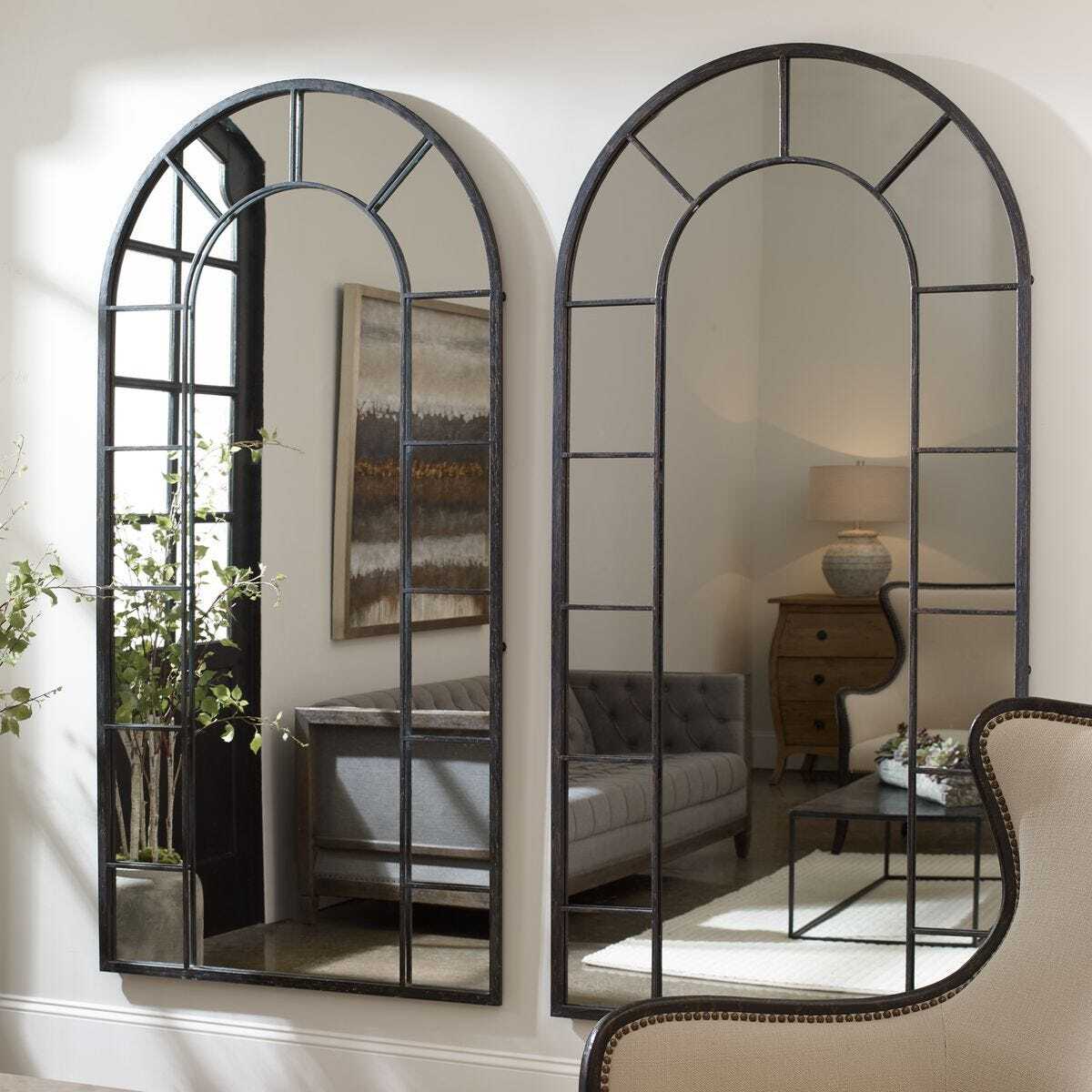Two large arched mirrors in a room with a sofa and lamp.