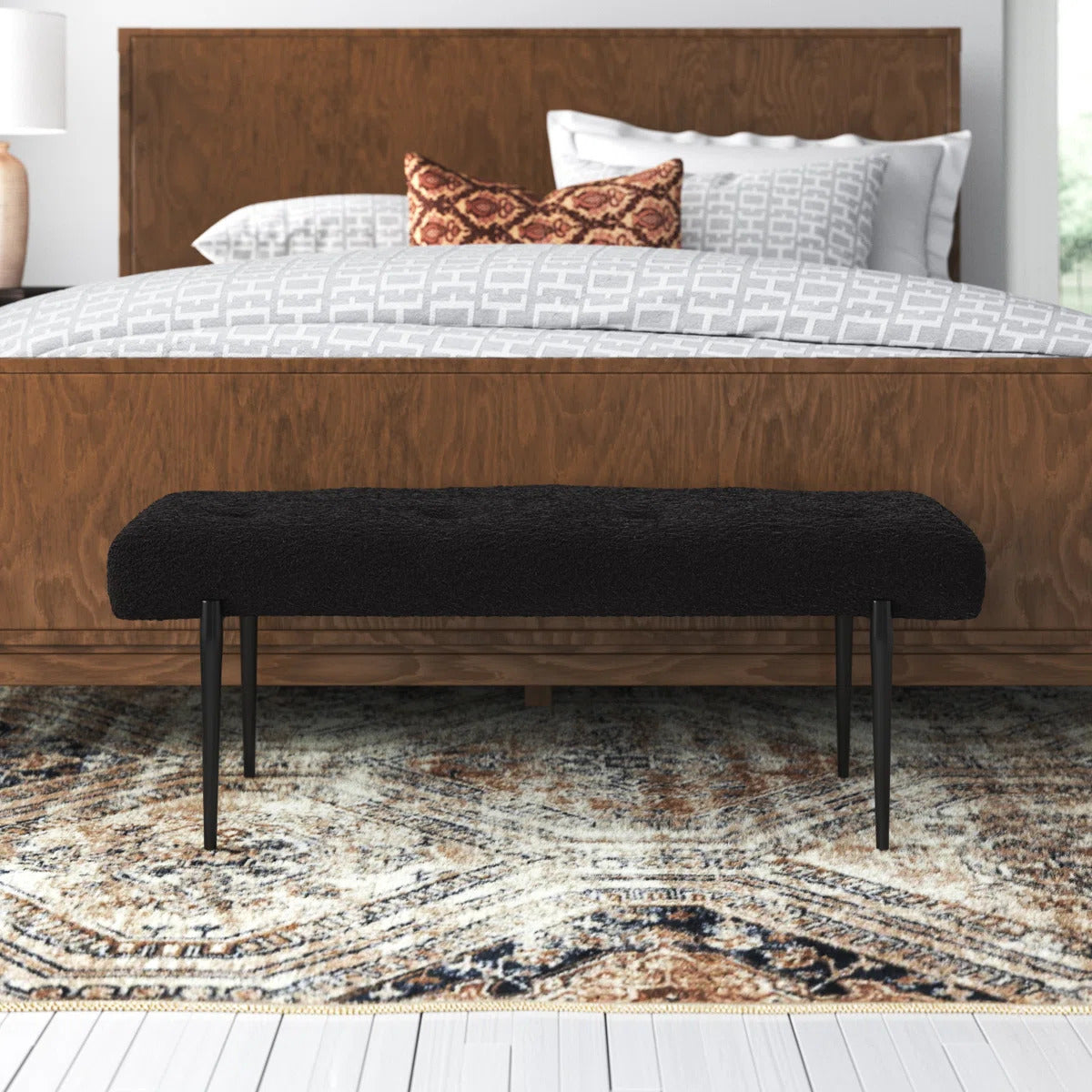 Wooden bed with white bedding and a black bench in front on a patterned rug.