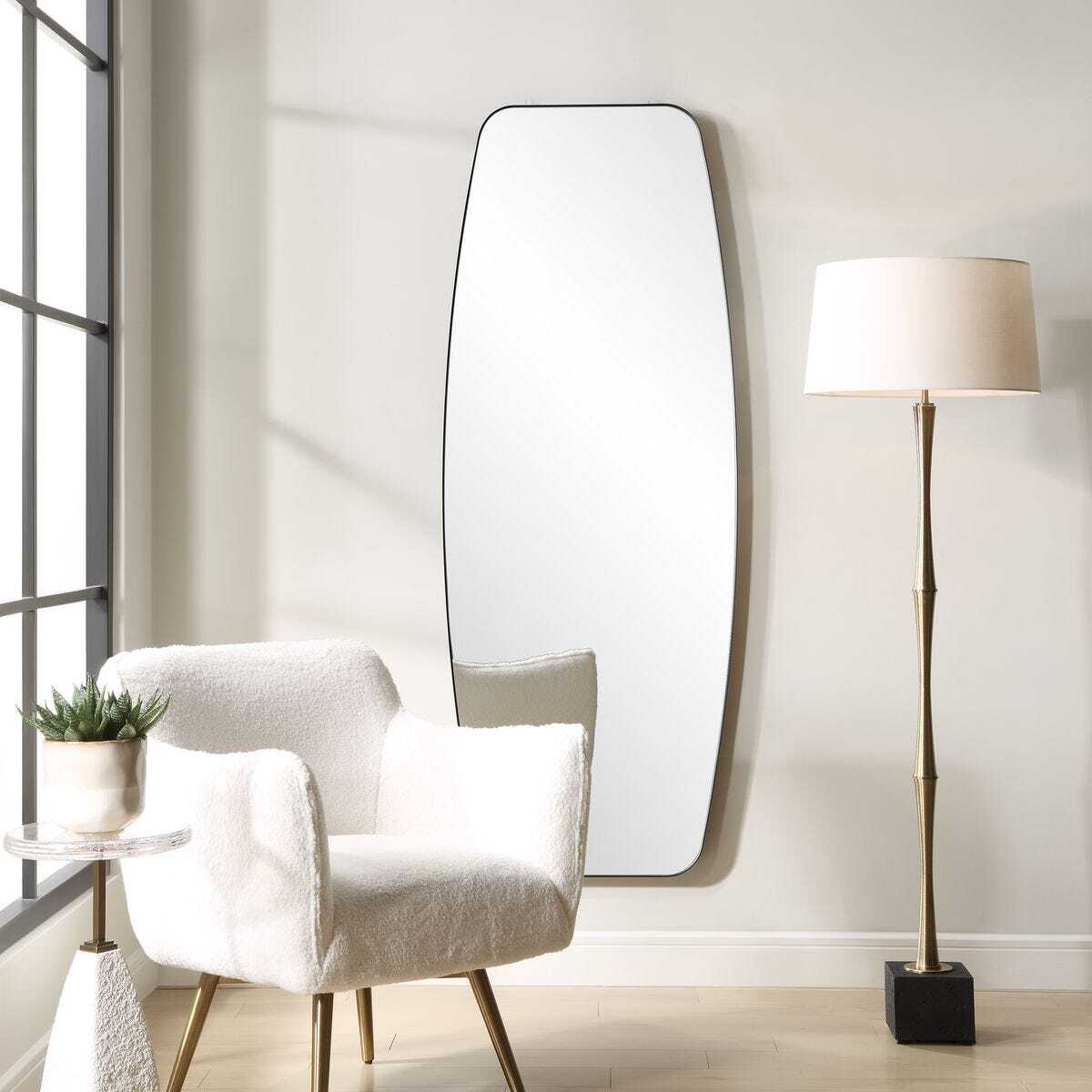Modern interior with a white armchair, floor lamp, and large mirror on a white wall.