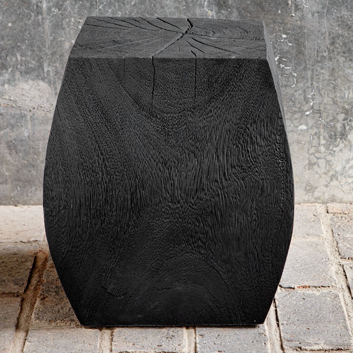 Black textured garden stool against a stone wall.